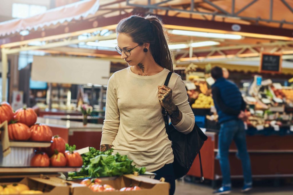 atractiva-mujer-joven-con-tatuaje-y-gafas-visitando-el-mercado-local-de-verduras-frescas_11zon