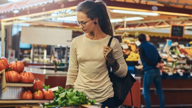 atractiva-mujer-joven-con-tatuaje-y-gafas-visitando-el-mercado-local-de-verduras-frescas_11zon